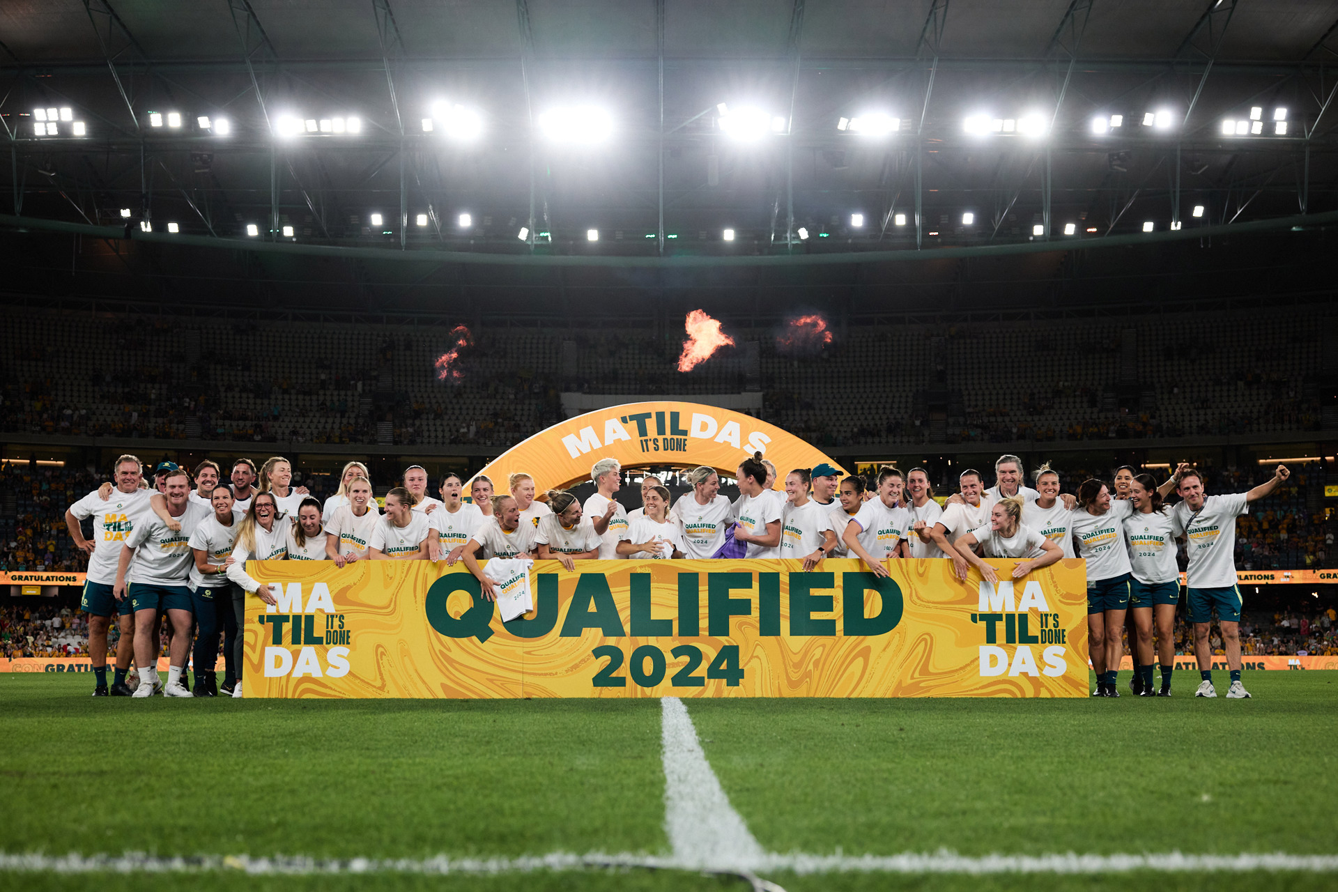 The soccer team hold a large yellow banner on the field that reads 'Qualified 2024'